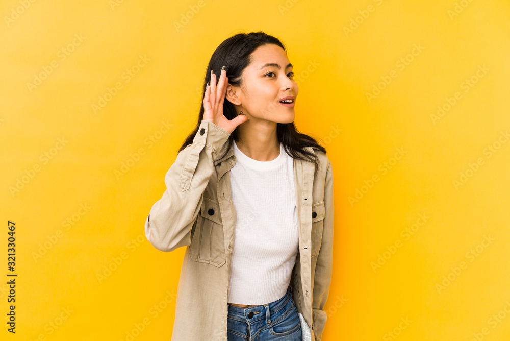 Young chinese woman isolated on a yellow background trying to listening a gossip. Young chinese woman isolated on a yellow background trying to listening a gossip.