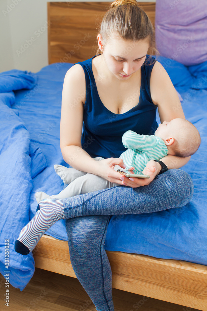 Fototapeta premium Mother using mobile phone while sitting with baby