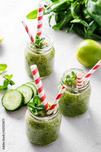 Jars with green smoothie and red tubules on a light background. Freshly made vegetable smoothie. Close-up. Glass jars with green smoothie on a concrete background.