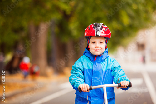 Cute preschooler boy in safety helmet riding a scooter.