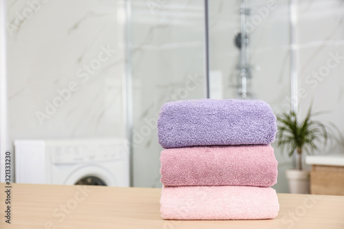 Stack of fresh towels on wooden table in bathroom. Space for text