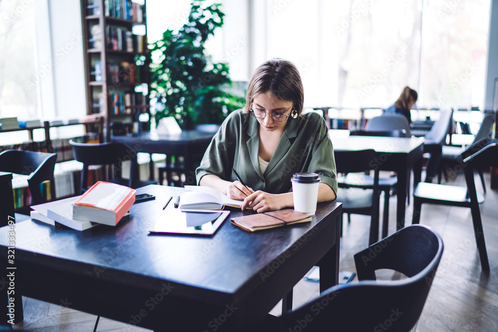 Diligent student in glasses writing in notepad Diligent student in glasses writing in notepad