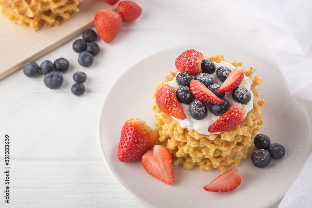 Delicious waffles with fresh fruit and berries on a white wooden table. Waffles with strawberries and blueberries. Free space for text. Traditional belgian waffles with fresh fruit. Stack of waffles w Delicious waffles with fresh fruit and berries on a white wooden table. Waffles with strawberries and blueberries. Free space for text. Traditional belgian waffles with fresh fruit. Stack of waffles w