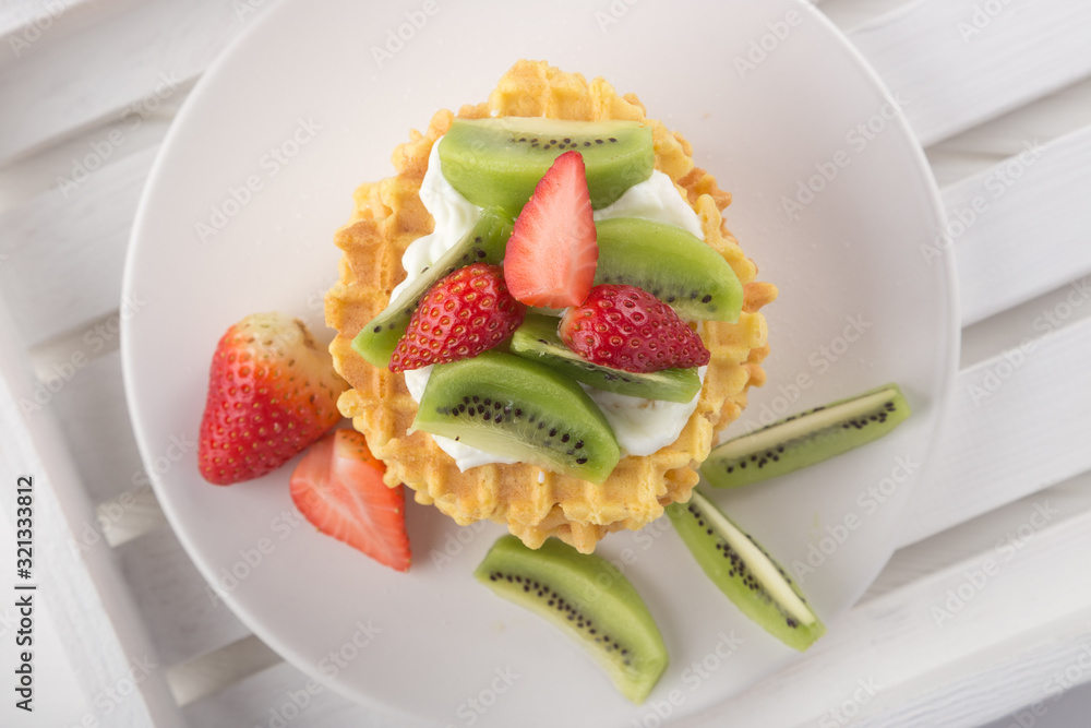 Delicious waffles with fresh fruit and berries on a white wooden table. Waffles with strawberries, kiwi, banana, cream. Free space for text. Traditional belgian waffles with fresh fruit. Stack of waff Delicious waffles with fresh fruit and berries on a white wooden table. Waffles with strawberries, kiwi, banana, cream. Free space for text. Traditional belgian waffles with fresh fruit. Stack of waff