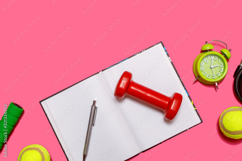 Healthy lifestyle concept with empty exercise book for text, fitness and sport. Tennis ball with dumbbells and green alarm clock isolated on pastel pink background. Healthy lifestyle concept with empty exercise book for text, fitness and sport. Tennis ball with dumbbells and green alarm clock isolated on pastel pink background.