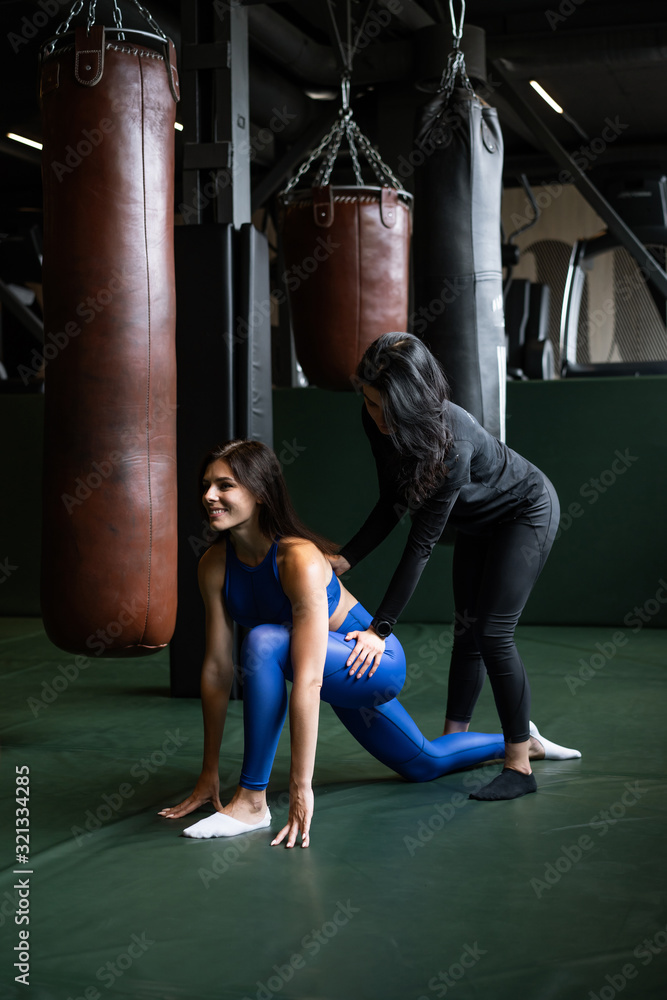 Two beautiful young girls doing fitness in a gym. Stretching the muscles of the back and legs.
