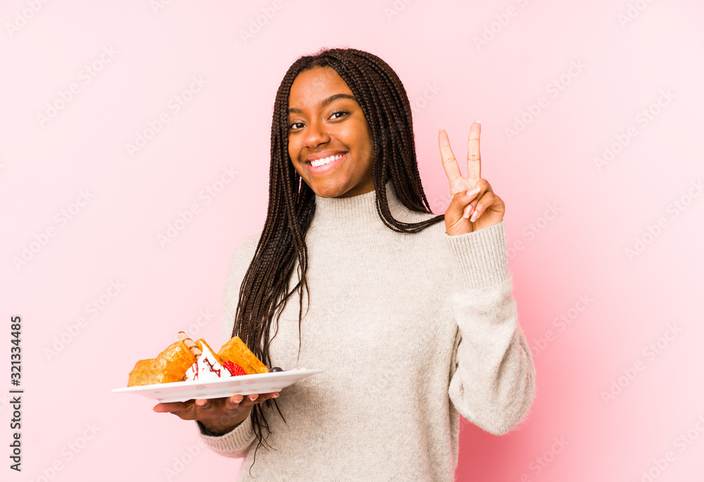 Young african american woman holding a waffle isolated showing number two with fingers. Young african american woman holding a waffle isolated showing number two with fingers.