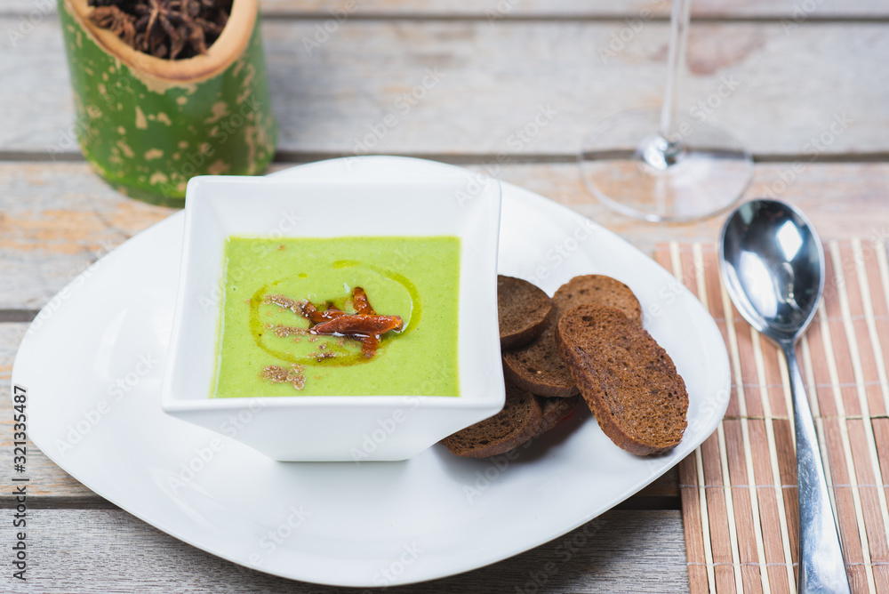 Green vegetarian broccoli cream soup with rye crackers on a wooden table in a restaurant or cafe. Green vegetarian broccoli cream soup with rye crackers on a wooden table in a restaurant or cafe.