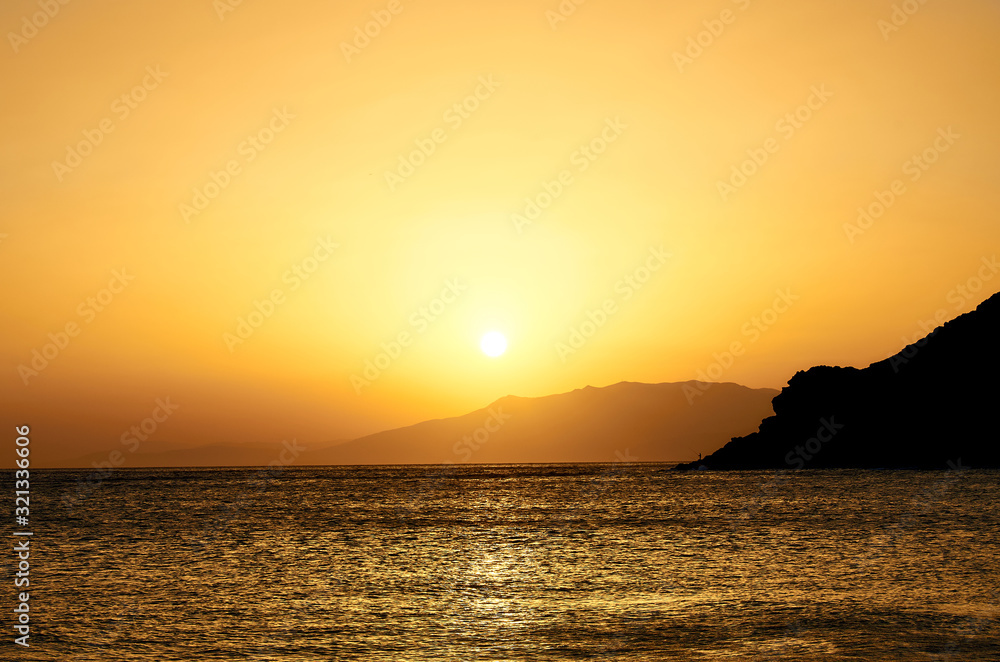 Landscape of a golden sunset in a beach in the Mediterranean. Sun disappearing behind the mountains.