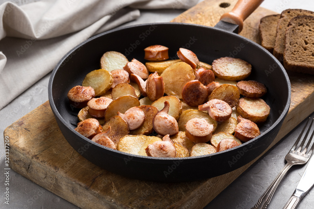 Close-up shot of fried potatoes with sausages and egg. Breakfast. Potatoes with sausages, cut into slices and fried in oil, in rustic style. Frying pan with tasty cooked egg and sausages on table Close-up shot of fried potatoes with sausages and egg. Breakfast. Potatoes with sausages, cut into slices and fried in oil, in rustic style. Frying pan with tasty cooked egg and sausages on table