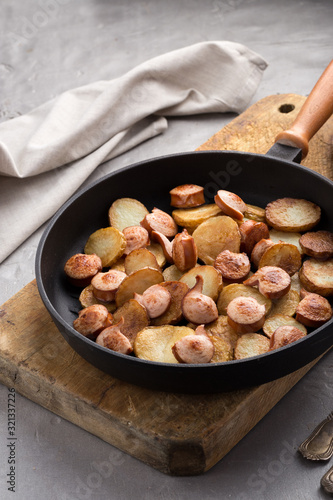 Close-up shot of fried potatoes with sausages and egg. Breakfast. Potatoes with sausages, cut into slices and fried in oil, in rustic style. Frying pan with tasty cooked egg and sausages on table