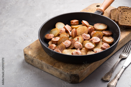 Close-up shot of fried potatoes with sausages and egg. Breakfast. Potatoes with sausages, cut into slices and fried in oil, in rustic style. Frying pan with tasty cooked egg and sausages on table