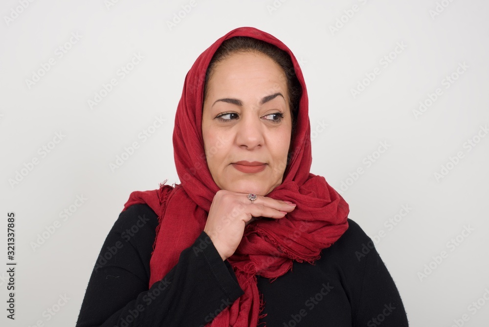 Dreamy female with pleasant expression, wearing casual clothes, looks sideways, keeps hand under chin, thinks about something pleasant, poses against gray background. Dreamy female with pleasant expression, wearing casual clothes, looks sideways, keeps hand under chin, thinks about something pleasant, poses against gray background.