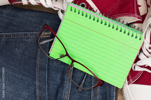 A pocket sized notebook is open on an empty page, freshly green color. Creative Flat Lay Composition with Glasses, Denim and Sneakers. Modern Background, Copy Space. Active & Stylish.  photo