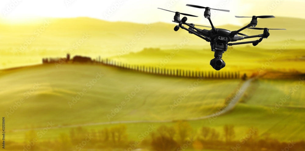 A flying drone with camera with blured hills of Tuscany in the background - obrazy, fototapety, plakaty 