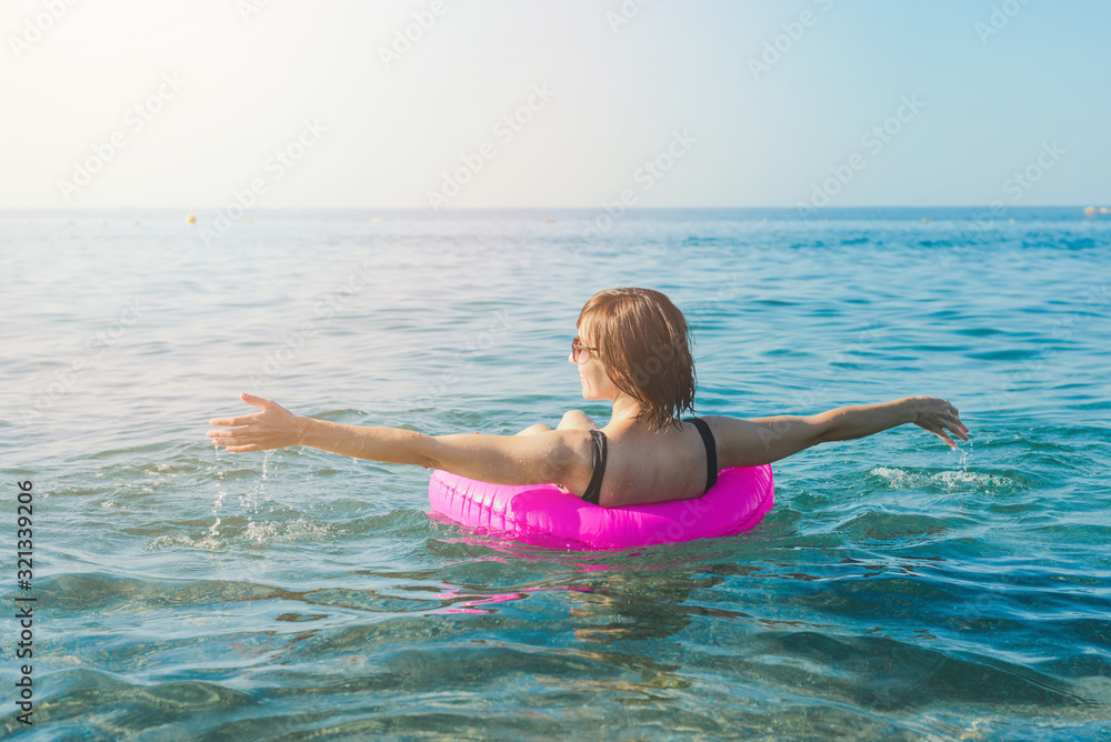 Young woman with pink swimming ring at the sea in sunny day. Summer vacation concept.