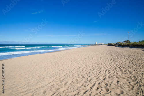 scenery of beautiful and lonely Palmar Beach with sand, turquoise ocean water and ancient tower in the horizon. In Vejer village (Cadiz, Andalusia, Spain)