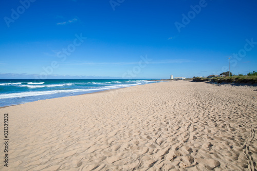 scenery of beautiful and lonely Palmar Beach with sand  turquoise ocean water and ancient tower in the horizon. In Vejer village  Cadiz  Andalusia  Spain 