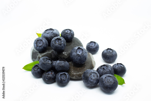 Blueberry berries with green leaves lie on the stones (pebbles) on a white background. Dew drops on blueberries