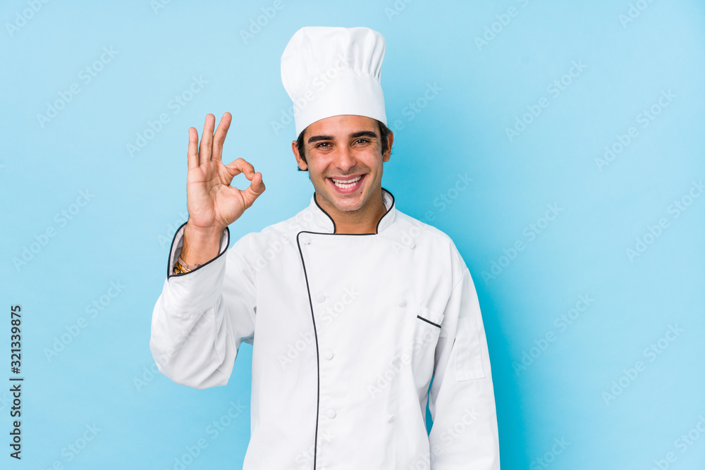 Young cook man isolated cheerful and confident showing ok gesture.