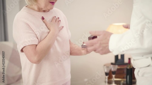 Unrecognizable senior Caucasian woman opening gift for Saint Valentine's Day. Happy wife getting new ring from husband. Romance, holiday, eternal love concept. photo