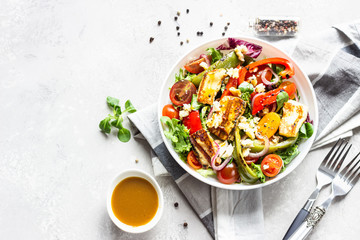 Vegetable salad cherry tomatoes, baked pepper, salad mix and onion with grilled haloumi (halloumi) cheese. Keto diet, healthy food. Light grey stone background. Top view.