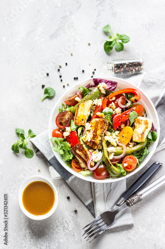 Vegetable salad cherry tomatoes, baked pepper, salad mix and onion with grilled haloumi (halloumi) cheese. Keto diet, healthy food. Light grey stone background. Top view.