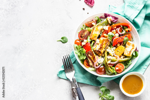 Vegetable salad cherry tomatoes, baked pepper, salad mix and onion with grilled haloumi (halloumi) cheese. Keto diet, healthy food. Light grey stone background.