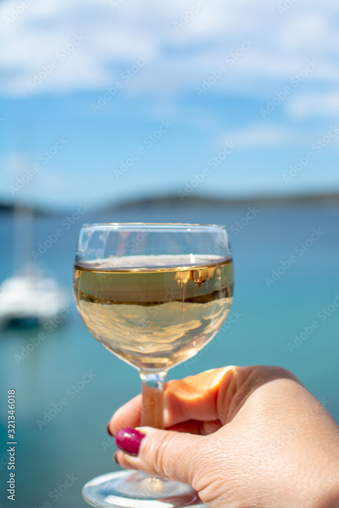 Woman hand with one glass of wine and blue sea view