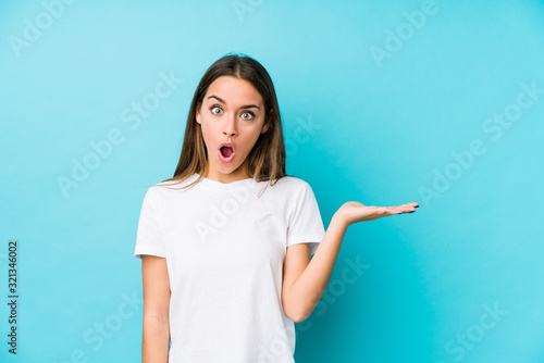 Young caucasian woman  isolated impressed holding copy space on palm.