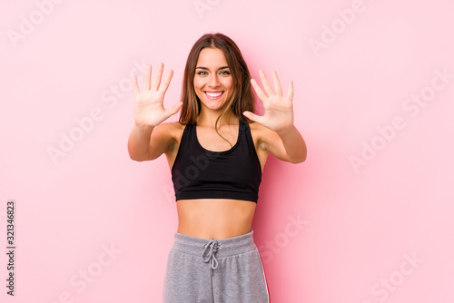 Young caucasian fitness woman posing in a pink background showing number ten with hands.