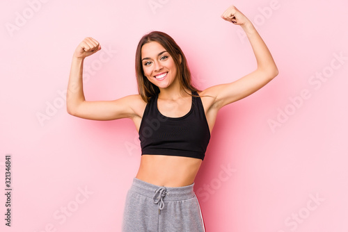 Young caucasian fitness woman posing in a pink background showing strength gesture with arms, symbol of feminine power