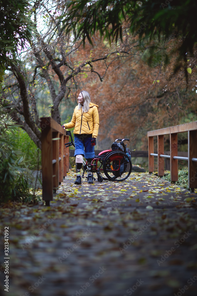 A strong woman without legs is standing on dentures next to a wheelchair.