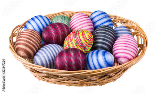 Colorful ornate Easter eggs pile in wicker basket isolated on white background. Hand-decorated striped egg shells wrapped by glued thin cotton sewing yarn. Ornate empty eggshells. Full depth of field.
