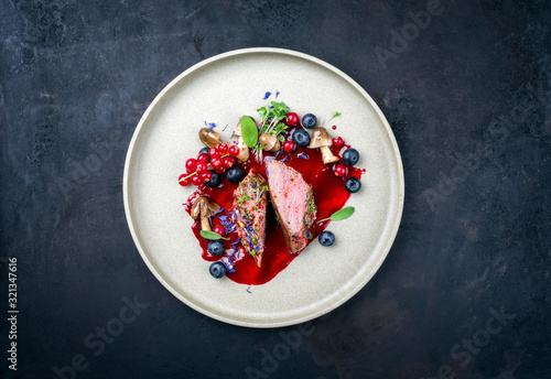 Fried dry aged venison tenderloin fillet medallion steak natural with mushrooms and forest berries as closeup on a modern design plate with copy space photo