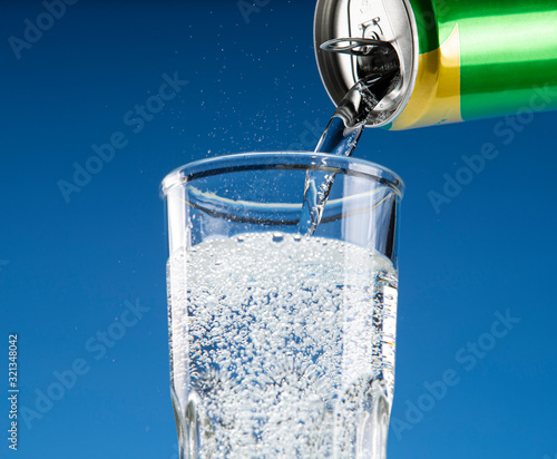 Carbonated drink pours from an aluminum can into a glass
