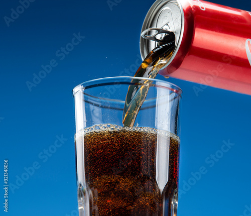 Carbonated drink pours from an aluminum can into a glass