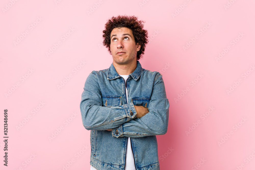 Curly mature man wearing a denim jacket against pink background tired of a repetitive task. Curly mature man wearing a denim jacket against pink background tired of a repetitive task.