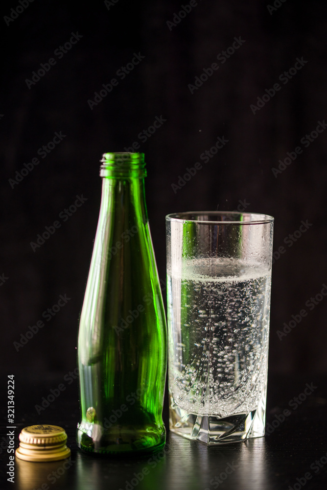 Mineral water in a high glass. Dark background with a bottle and a glass of water.
