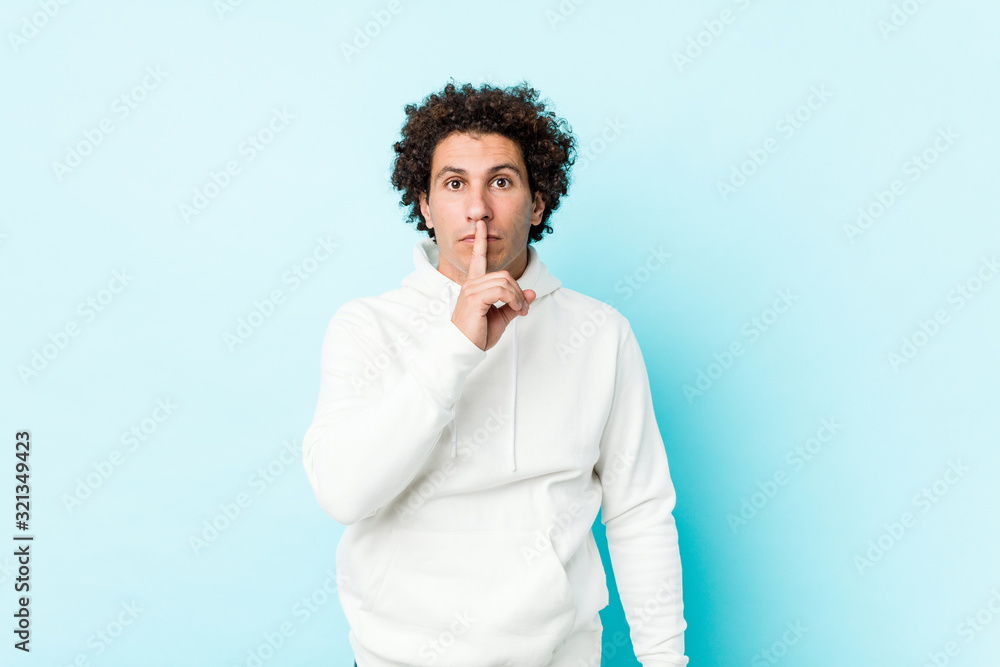 Young sporty man against a blue background keeping a secret or asking for silence. Young sporty man against a blue background keeping a secret or asking for silence.