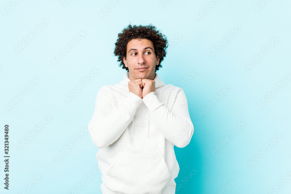 Young sporty man against a blue background keeps hands under chin, is looking happily aside. Young sporty man against a blue background keeps hands under chin, is looking happily aside.