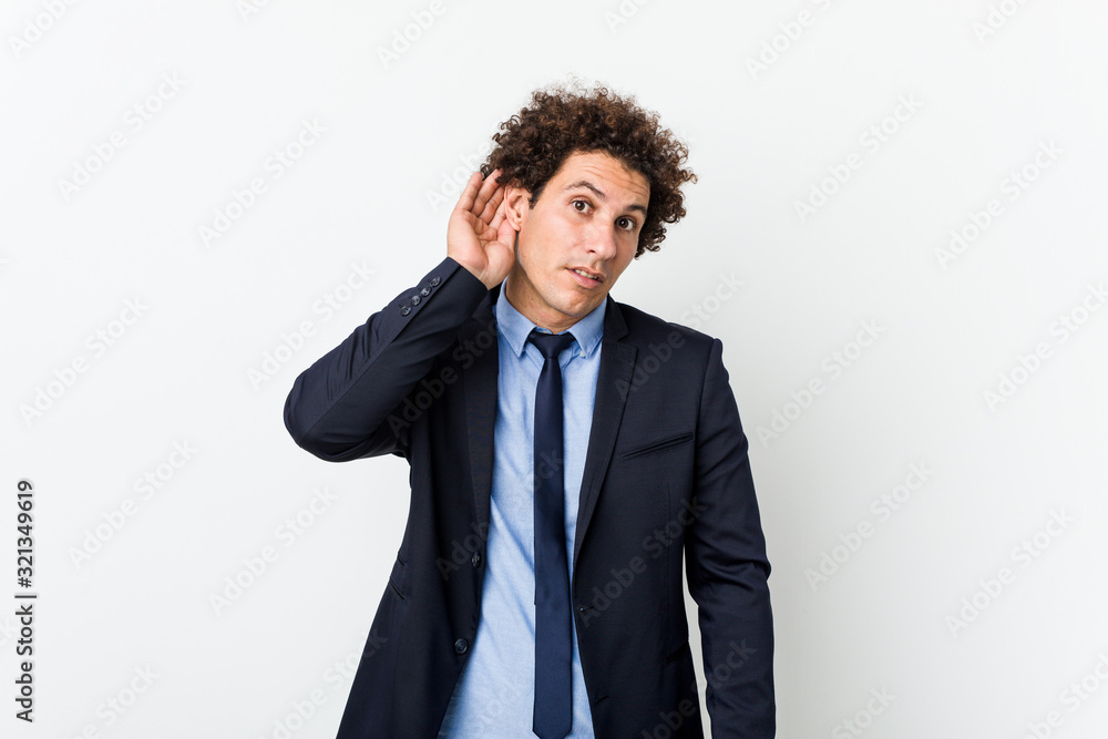 Young business curly man against white background trying to listening a gossip. Young business curly man against white background trying to listening a gossip.