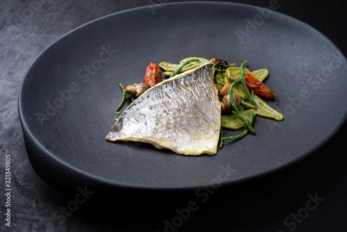 Gourmet fried Italian gilthead fish filet with spinach pasta, glasswort and tomatoes as closeup on a modern design plate photo