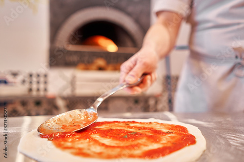 Cooking pizza. the workpiece poured tomato sauce. Closeup hand of chef. Baker in uniform and white apron cooking at kitchen