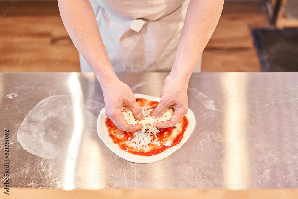 Cooking pizza. arranges cheese ingredients on the dough preform. Closeup hand of chef baker in uniform white apron cook at kitchen