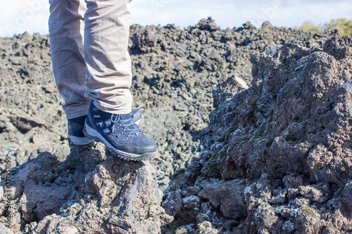 top view of trekking shoes on the lava stone background, male legs.