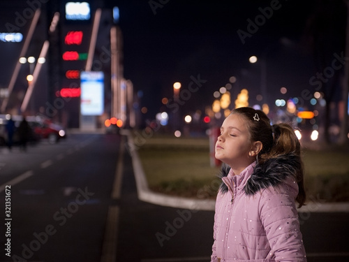 Obraz na plátně Little girl with closed eyes staying in dark in front of shopping mall lights