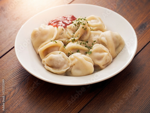 Portion of Russian classic big size dumplings on a white plate with tomato ketchup and herbs. Dark wood table surface.