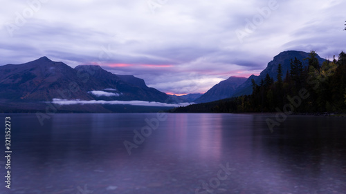 Sunrise over lake at Glacier National Park. Purlpe tinted cloudy morning