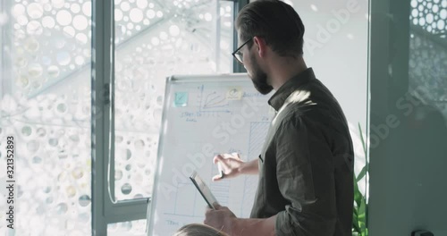Portrait of Attractive Speaker Standing by Board with Marker and Tablet in his Hands, Looking Confident. Having Speak about new Projects and Proposing his Ideas. Teamwork. Business Lifestyle.